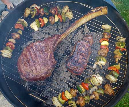 烤架上的战斧牛排和蔬菜串。