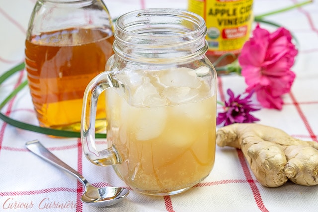 加勒比双切 - 蜂蜜生姜饮料 - 在一个罐子蜂蜜包围的一个手德玻璃杯子里蜂蜜和一块姜