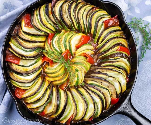 分层ratatouille的顶上的图象在铸铁煎锅的与茄子，夏天南瓜，夏南瓜，蕃茄和红辣椒。
