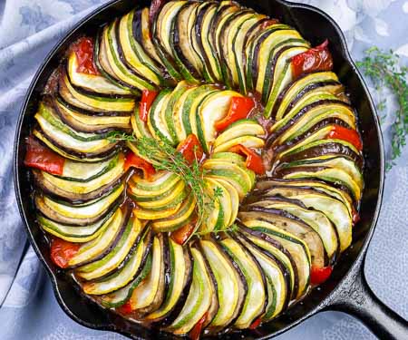 头顶上的图像是在铸铁煎锅里分层的蔬菜杂烩，里面有茄子、西葫芦、西葫芦、西红柿和红辣椒。