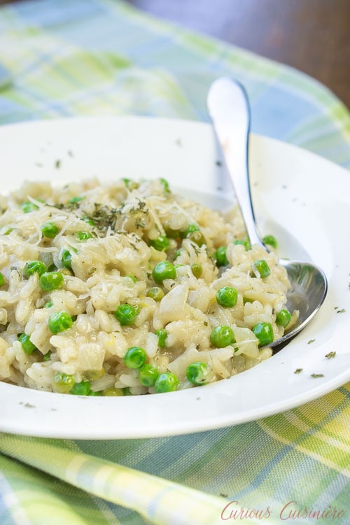 奶油春天豌豆烩饭在一个白色的碗和勺子。gydF4y2Ba