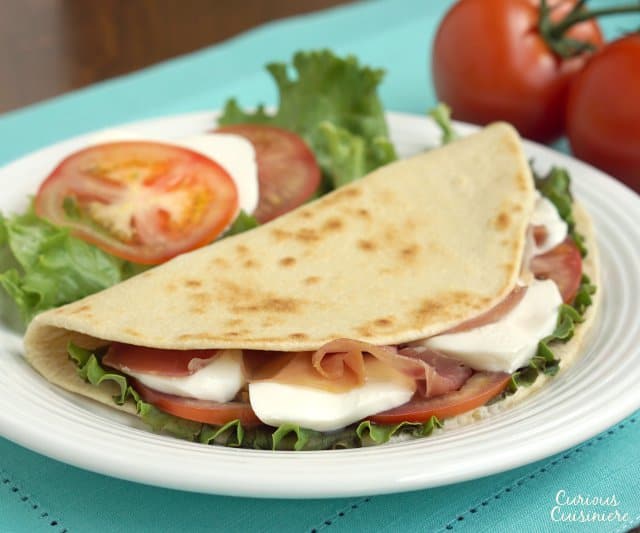 Piadina是一种薄的意大利面饼，由街头小贩制作，像三明治一样出售，里面塞满了新鲜的马苏里拉奶酪和美味的熏火腿等美味的馅料。| www.CuriousCuisiniere.com